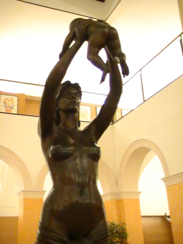 Escultura en bronce de una mujer sosteniendo a un niño en alto