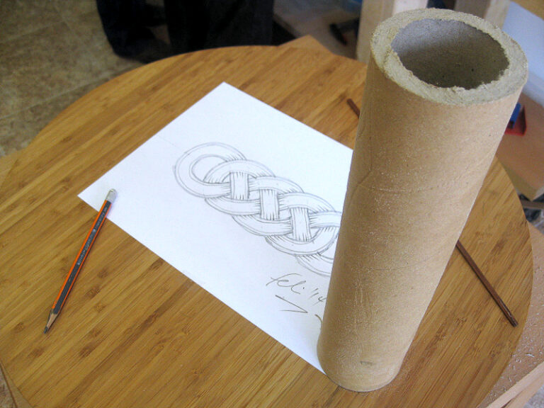 Dibujo de una trenza celta sobre papel, junto a un tubo de cartón
