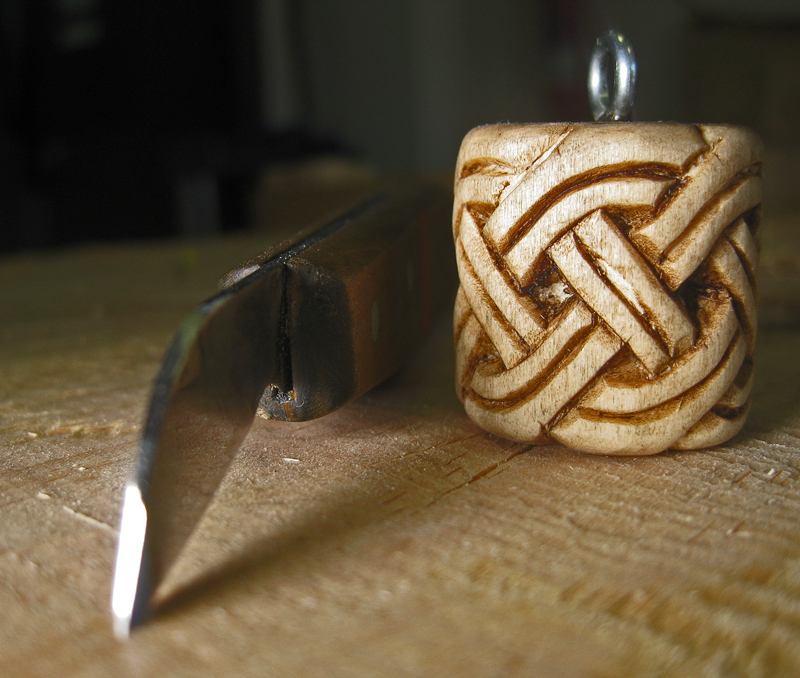 Cilindro de tilo decorado con una trenza celta, junto a una gubia