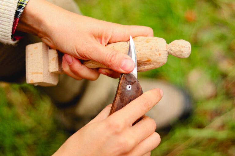 Manos tallando una figura de madera con un cuchillo, al aire libre